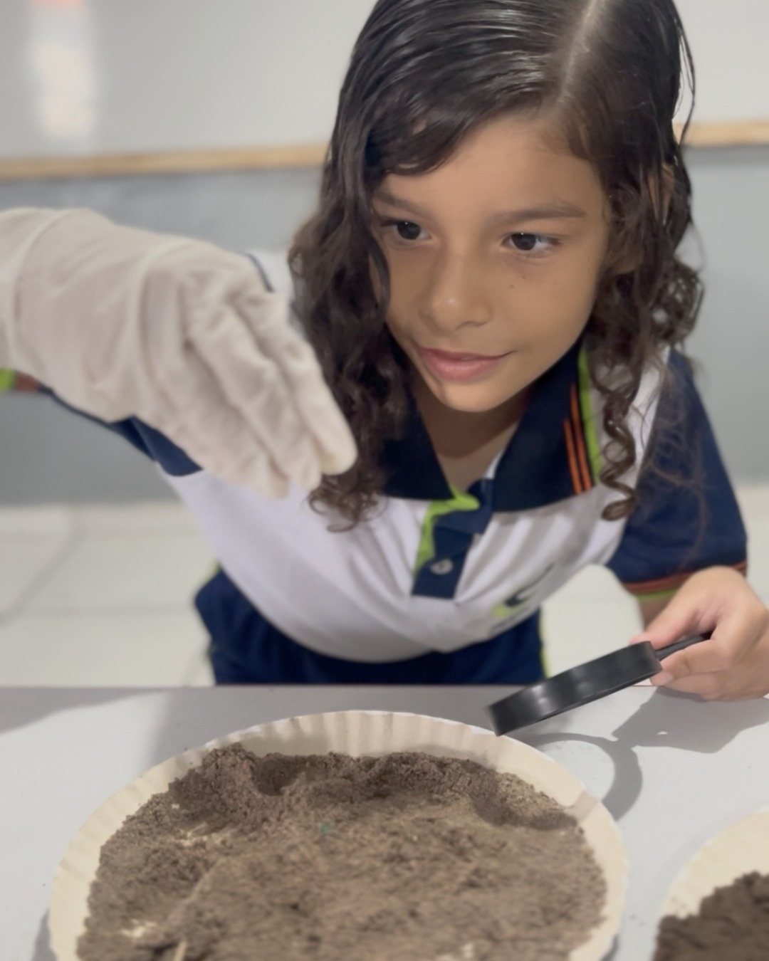 Aluna analisando amostra de solo com lupa na aula de ciências
